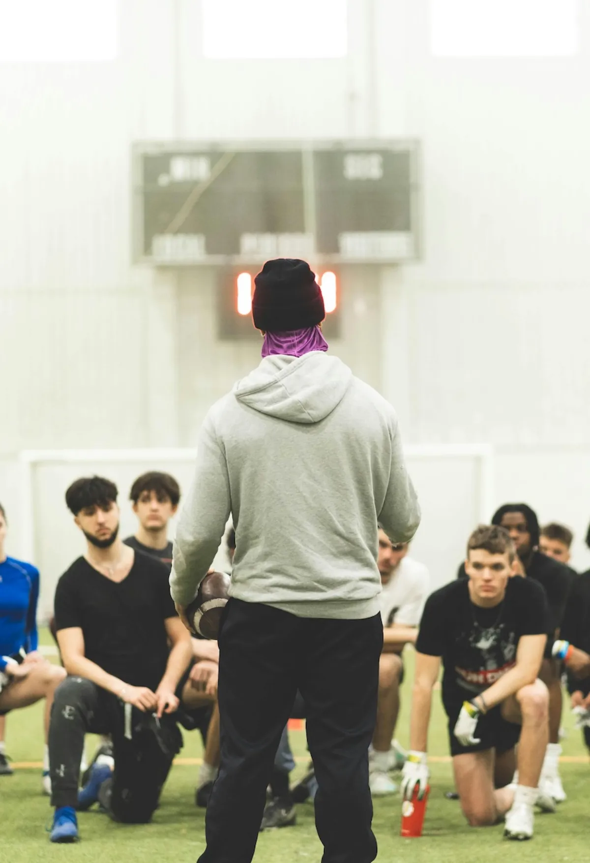 Coach addressing a group of young athletes kneeling on a turf field