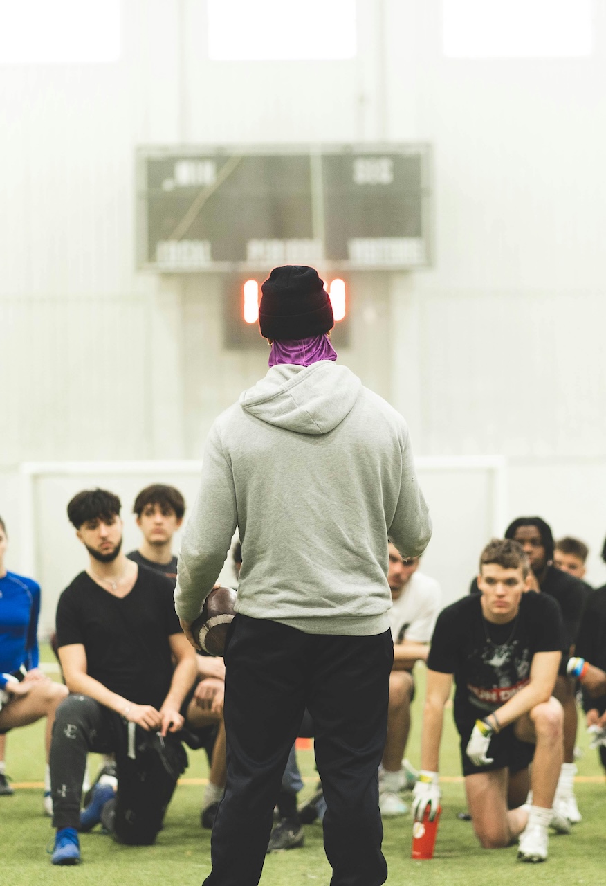 Coach addressing a group of young athletes kneeling on a turf field