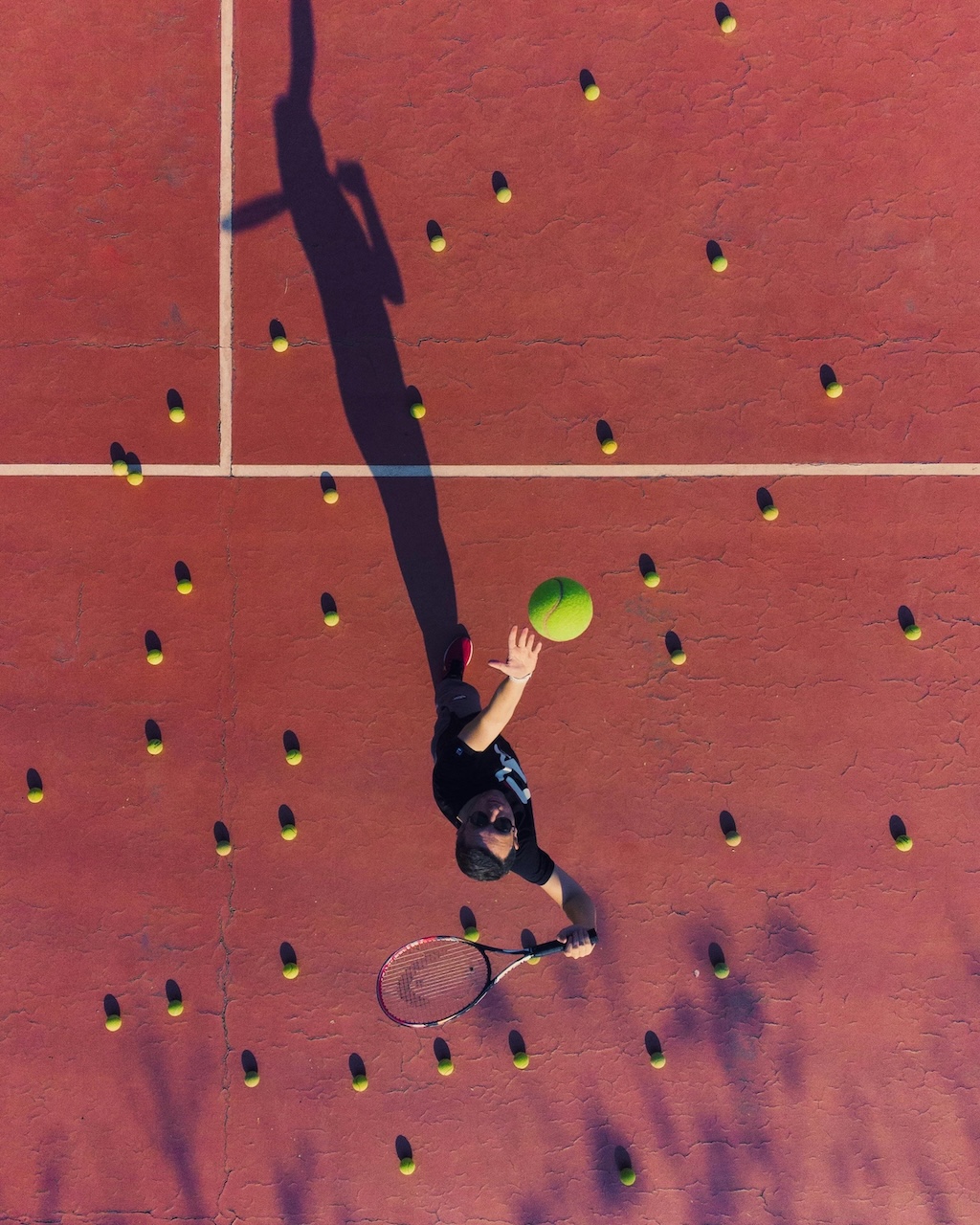 Overhead view of a tennis player on court surrounded by scattered balls